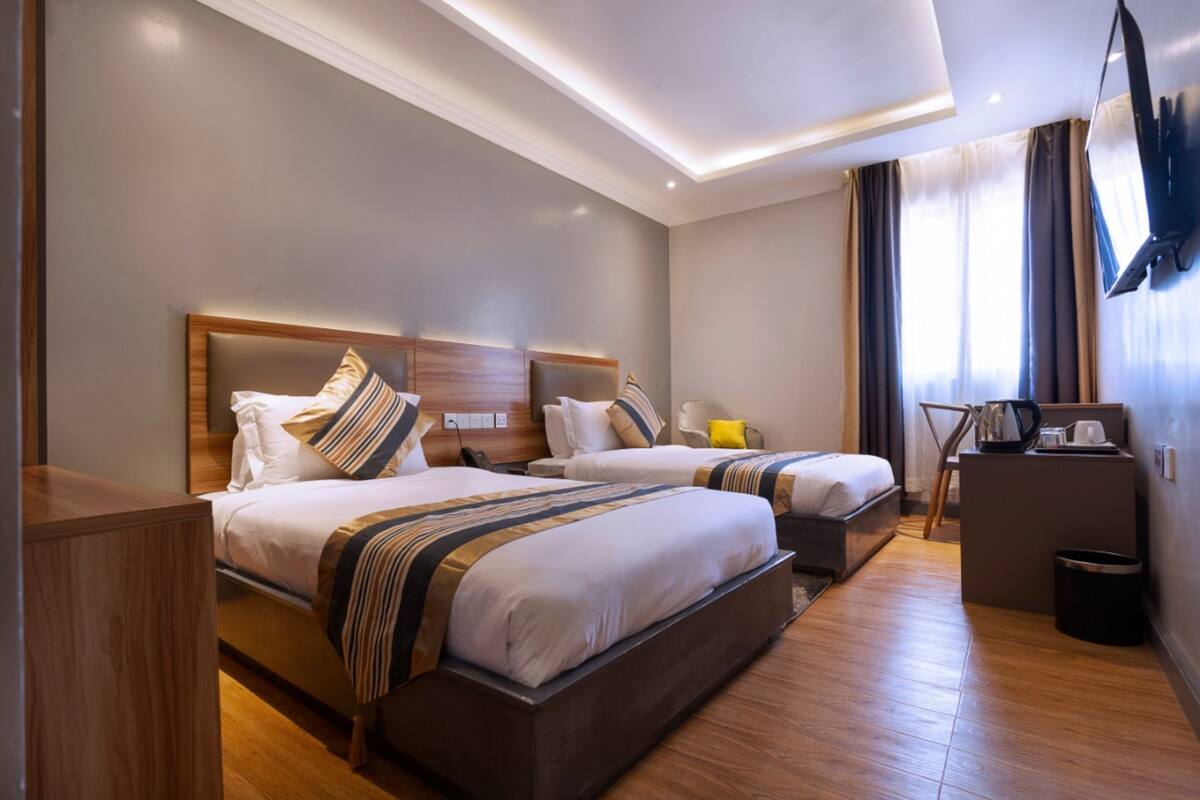 A hotel room with two beds, a wooden headboard, a small desk, and a TV mounted on the wall.