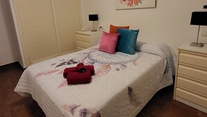 Un dormitorio con cama, mesita de noche, cómoda, armario y lámpara de pared.