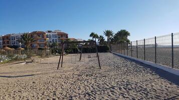 Enjoy leisure time on the beach with a wooden swing set and fenced area, surrounded by Mediterranean-style buildings with balconies.