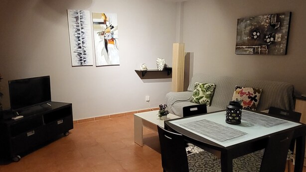 A dining area with a table set for two, a black TV stand, and artwork on the walls. - Beautiful low house with private naturist garden! (Vera)