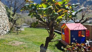 Un jardin avec un petit arbre, une maison de jeu colorée et un mur en pierre.