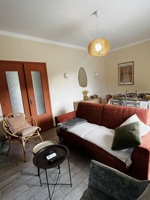 A living room with a sofa, a chair, a small table, and a dining area with a table set for four.