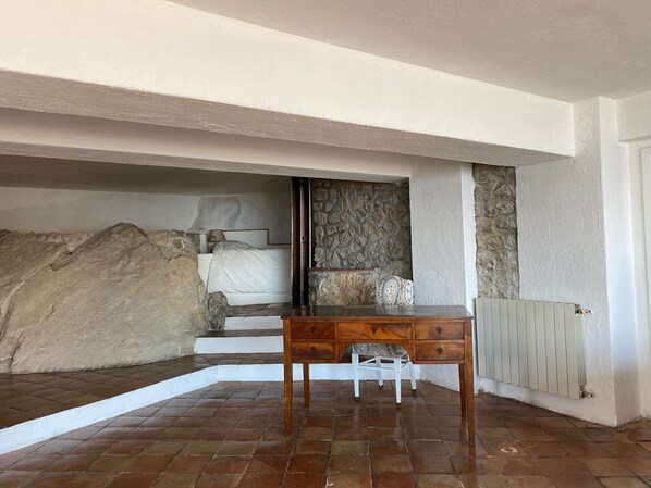 A bedroom with a stone wall, a bed, a wooden nightstand, and a radiator. - La Casa nella roccia (Taormina)