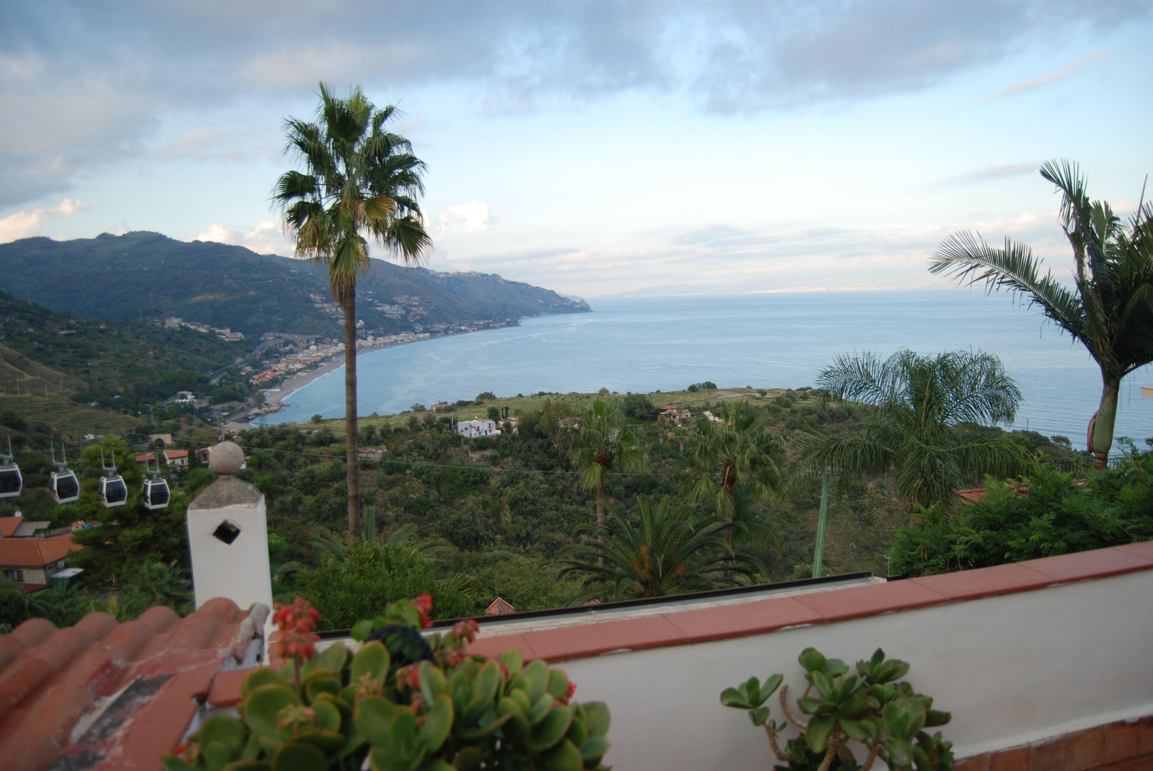 Una vista sulla costa con montagne sullo sfondo, un edificio bianco con un campanile e una palma.