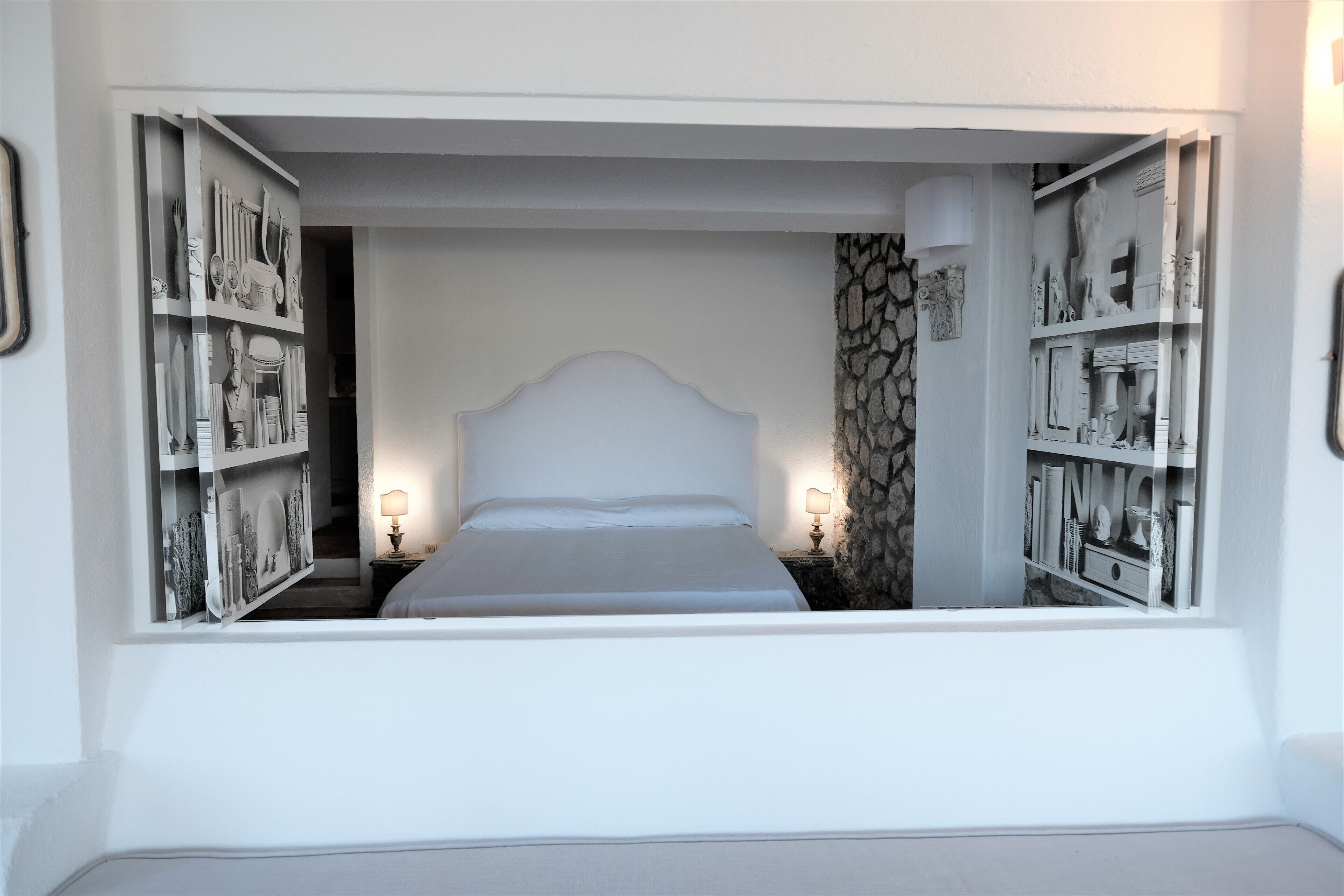 A bedroom with a large bed, two bedside tables with lamps, and a stone accent wall.
