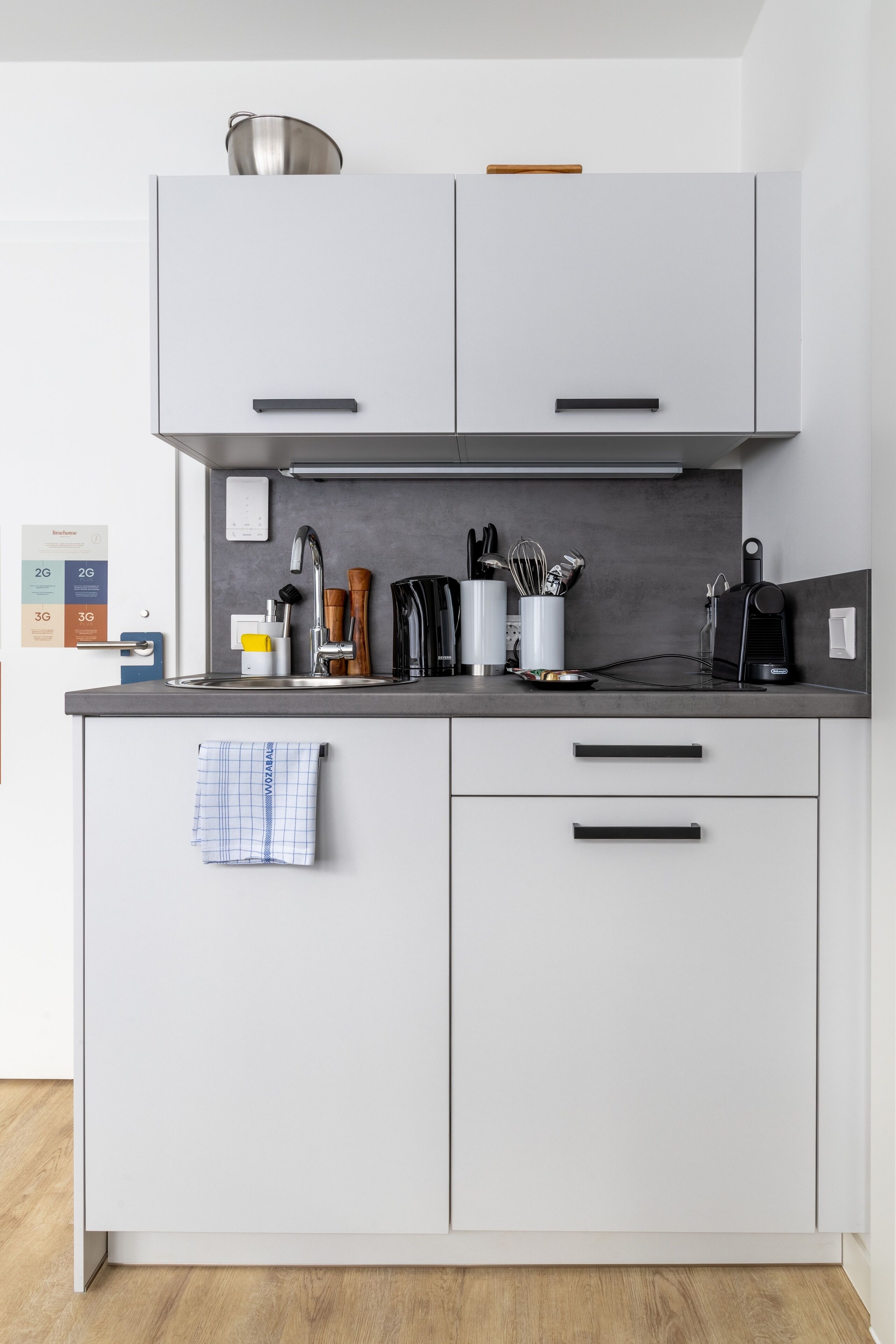 A modern kitchen with white cabinets, a black countertop, and various kitchen utensils.