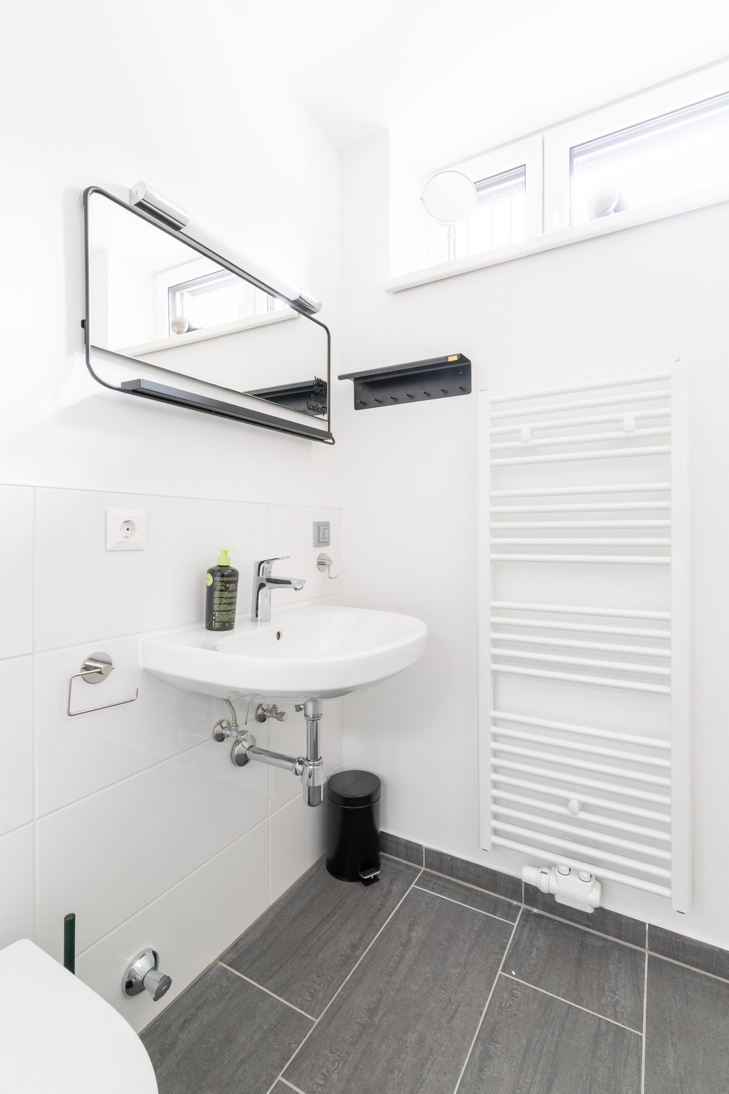 A modern bathroom with a white sink, mirror, and radiator.