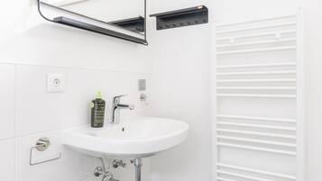 Un baño moderno con lavamanos, espejo y radiador blancos.
