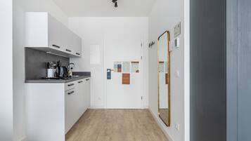 A modern kitchen with white cabinets, a wooden countertop, and a built-in oven. There is a mirror on the wall and a door with informational posters.