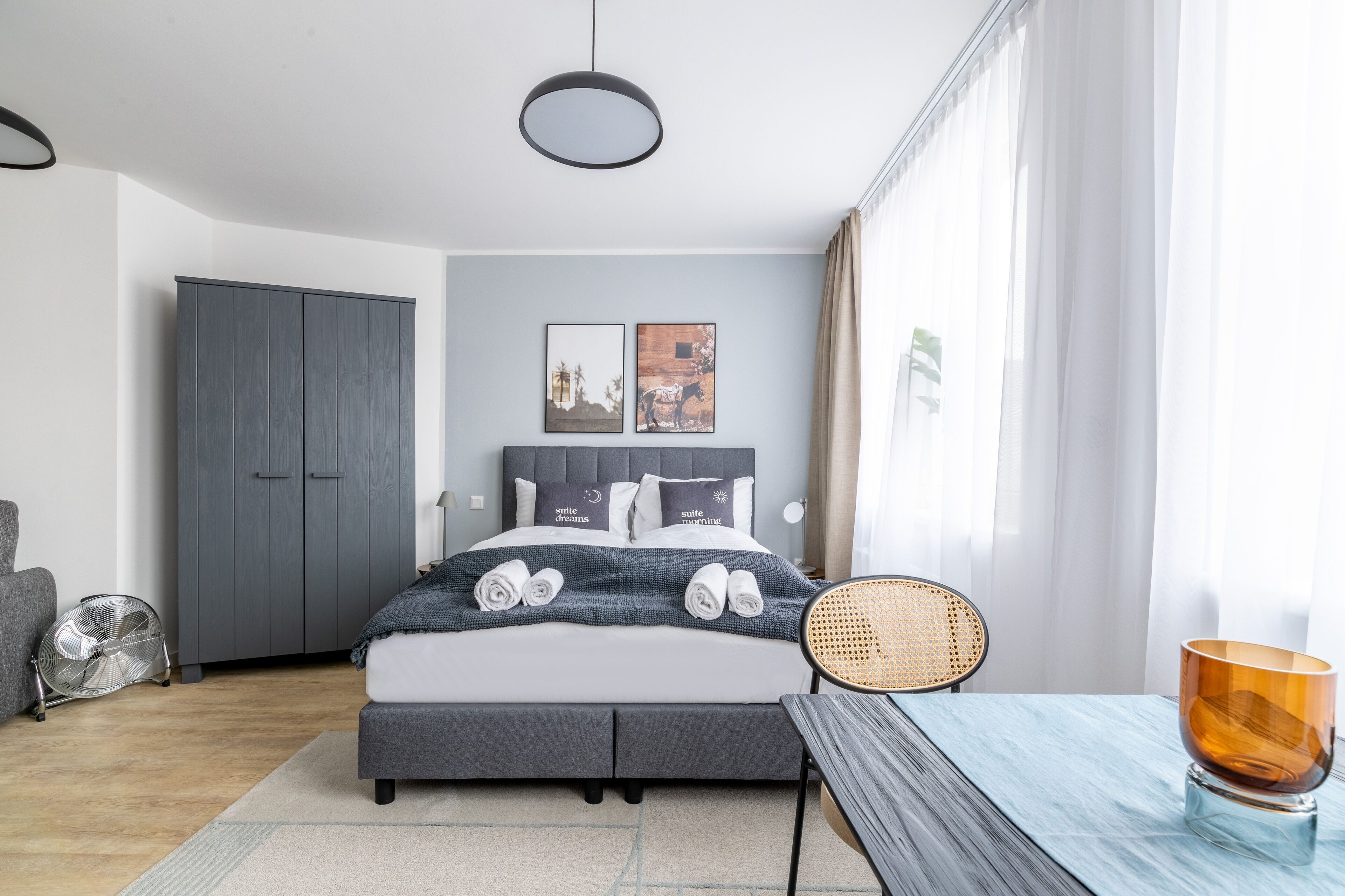 A modern bedroom with a bed, bedside table, chair, and a fan.