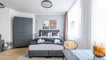 A modern bedroom with a bed, bedside table, chair, and a fan.