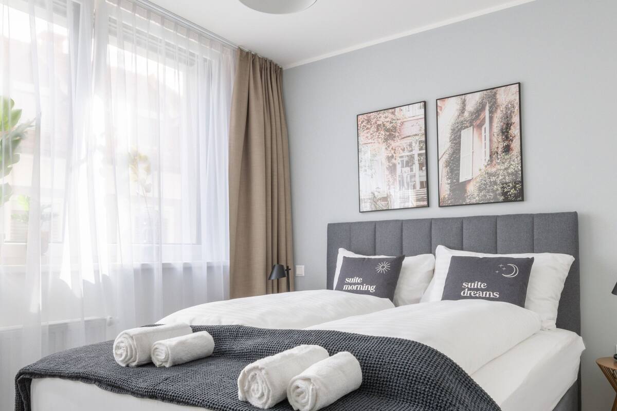 Une chambre moderne avec un grand lit, une literie grise et deux œuvres d’art accrochées au mur.