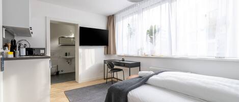 A modern hotel room with a bed, a desk, and a kitchenette.