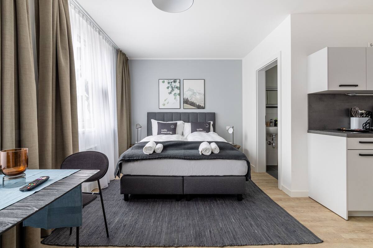 Une chambre d’hôtel moderne équipée d’un lit, d’un bureau, d’une chaise et d’une kitchenette.