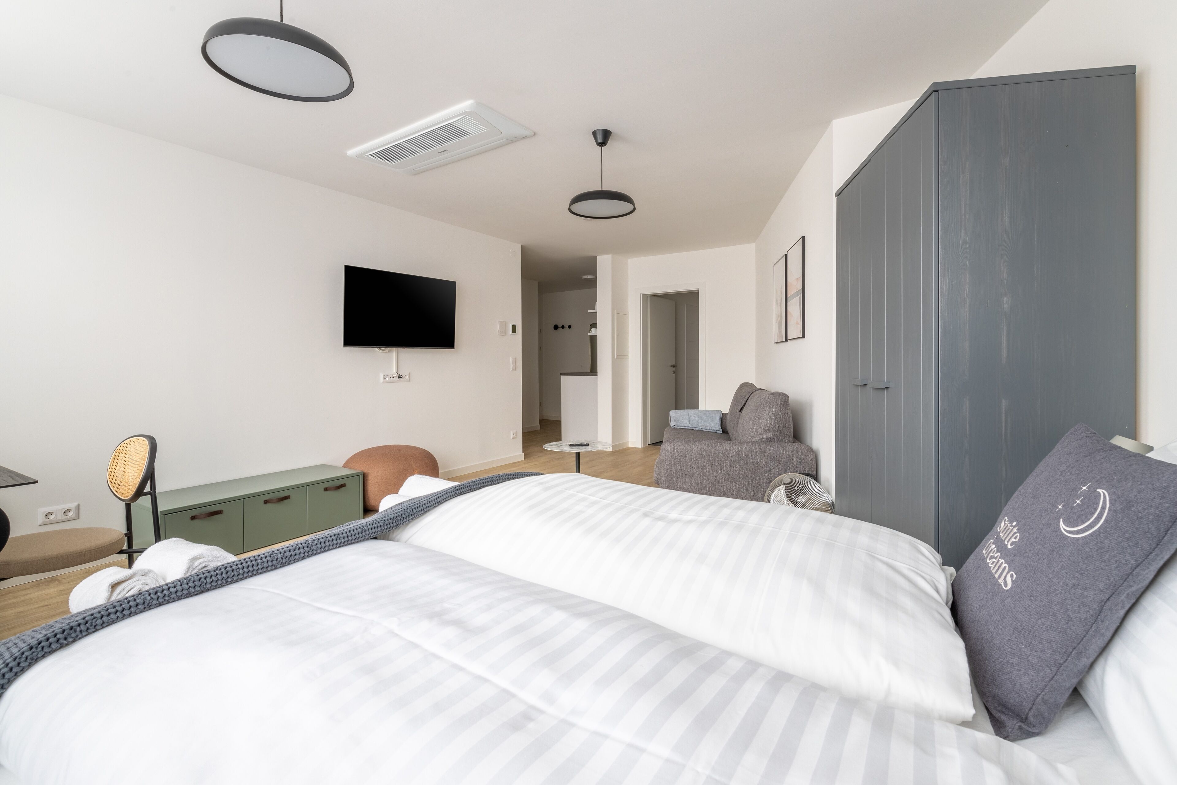 A modern bedroom with a large bed, a flat-screen TV, a wardrobe, and a desk with a chair.