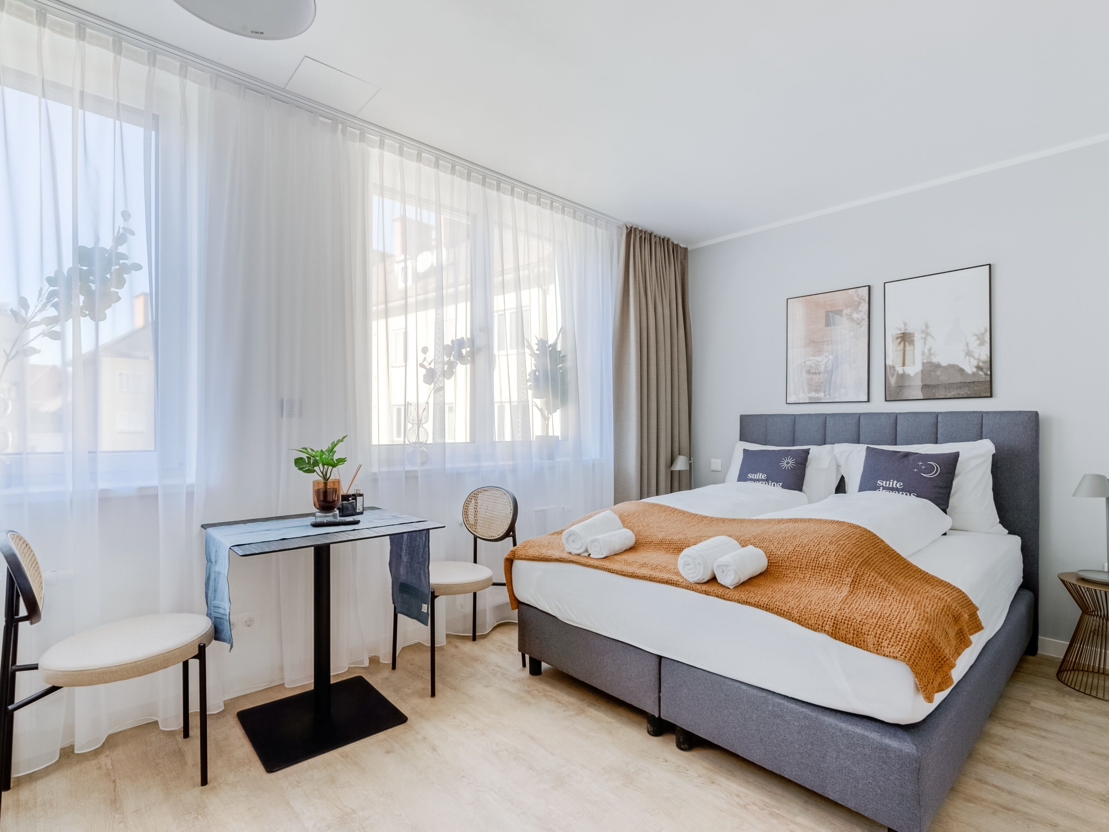 Camera d'albergo moderna con un letto grande, una scrivania, una sedia e vista all'esterno attraverso tende leggere.
