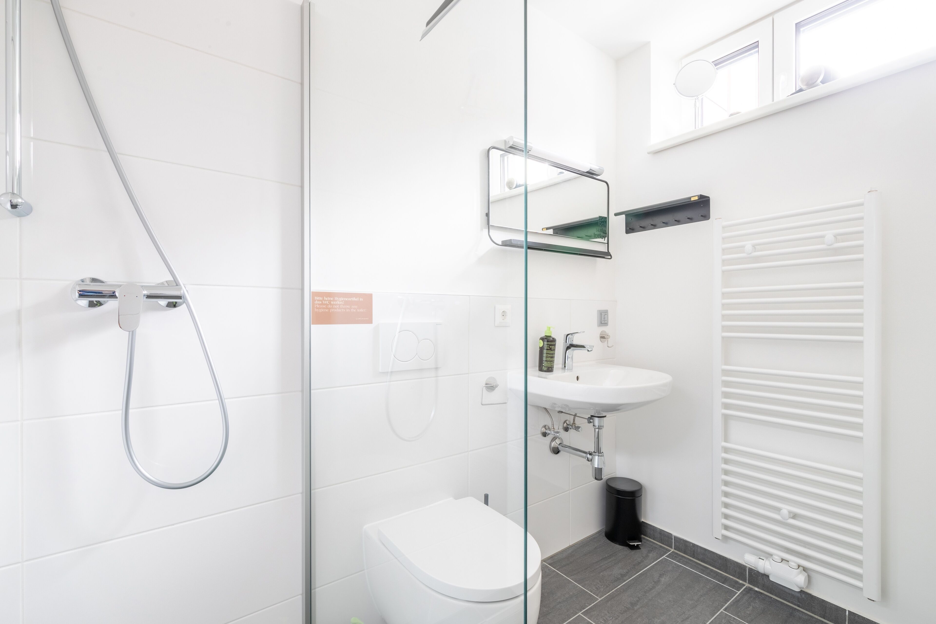 Un baño moderno con cabina de ducha de vidrio, inodoro blanco, lavamanos y radiador.