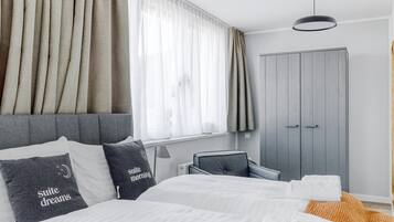 A modern hotel room with a large bed, grey wardrobe, and a window with sheer curtains.
