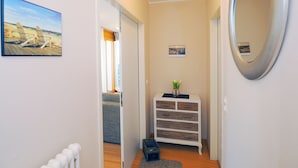 A hallway with a wooden floor, a white radiator, a mirror, a small plant on a white dresser, and a painting of a beach scene. - Apartment with 1 bedroom and balcony (Seebad Heringsdorf)