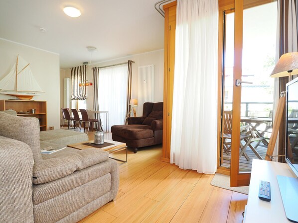 A living room with a sofa, armchair, dining area, and a view through a sliding door to an outdoor deck.