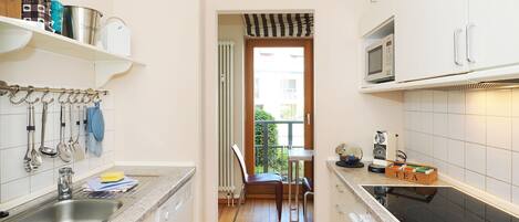 A narrow kitchen with a sink, stove, and cabinets. There is a window with a view of the outside.