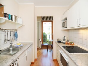 A narrow kitchen with a sink, stove, and cabinets. There is a window with a view of the outside.
