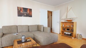 A living room with a sectional sofa, a coffee table, a bookshelf, and a sailboat model. - Apartment with 1 bedroom and balcony (Seebad Heringsdorf)