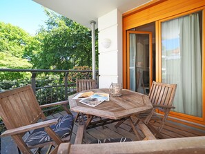 A wooden table and chairs on a balcony with a view of greenery.