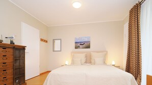 A bedroom with a large bed, wooden dresser, and a painting on the wall. - 1-room apartment with terrace (Seebad Heringsdorf)