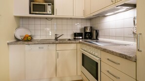 A compact kitchen with white cabinets, a microwave, a coffee maker, and a dishwasher. - 1-room apartment with terrace (Seebad Heringsdorf)