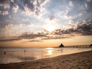 Une plage avec une jetée qui s’avance dans des eaux calmes, un ciel dégagé et un coucher de soleil.