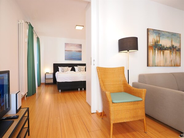 A modern hotel room with a bed, a chair, a sofa, a painting, and a lamp.
