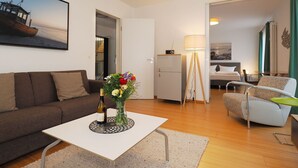 Ein modernes Wohnzimmer mit einer Couch, einem Couchtisch mit Blumen, einem wandmontierten Flachbildfernseher und einem Essbereich mit Tisch und Stühlen.