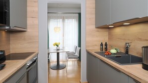 Eine moderne Küche mit grauen Schränken, einer Holz Arbeitsplatte und einem eingebauten Backofen. Es gibt einen Essbereich mit Tisch und Stühlen sowie ein Fenster mit transparenten Vorhängen.
