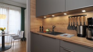 Eine moderne Küche mit grauen Schränken, einer Holzausziehtafel und einer Edelstahl-Spüle. An der Wand hängen Küchenutensilien, ein Kaffeeautomat steht auf der Arbeitsfläche, sowie ein Buch.
