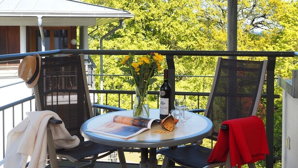 A balcony with a round table, two chairs, a bottle of wine, and a vase with flowers.