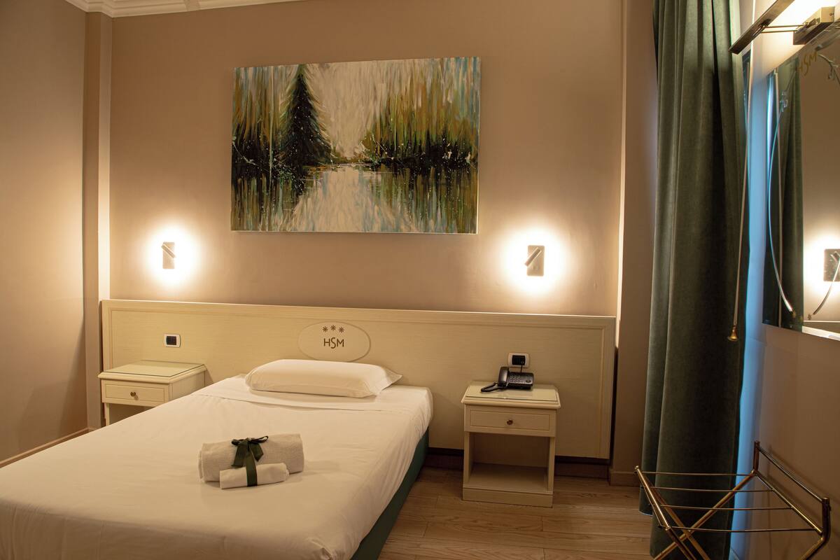 Una habitación de hotel con una cama, mesitas de noche, un cuadro y una cortina.
