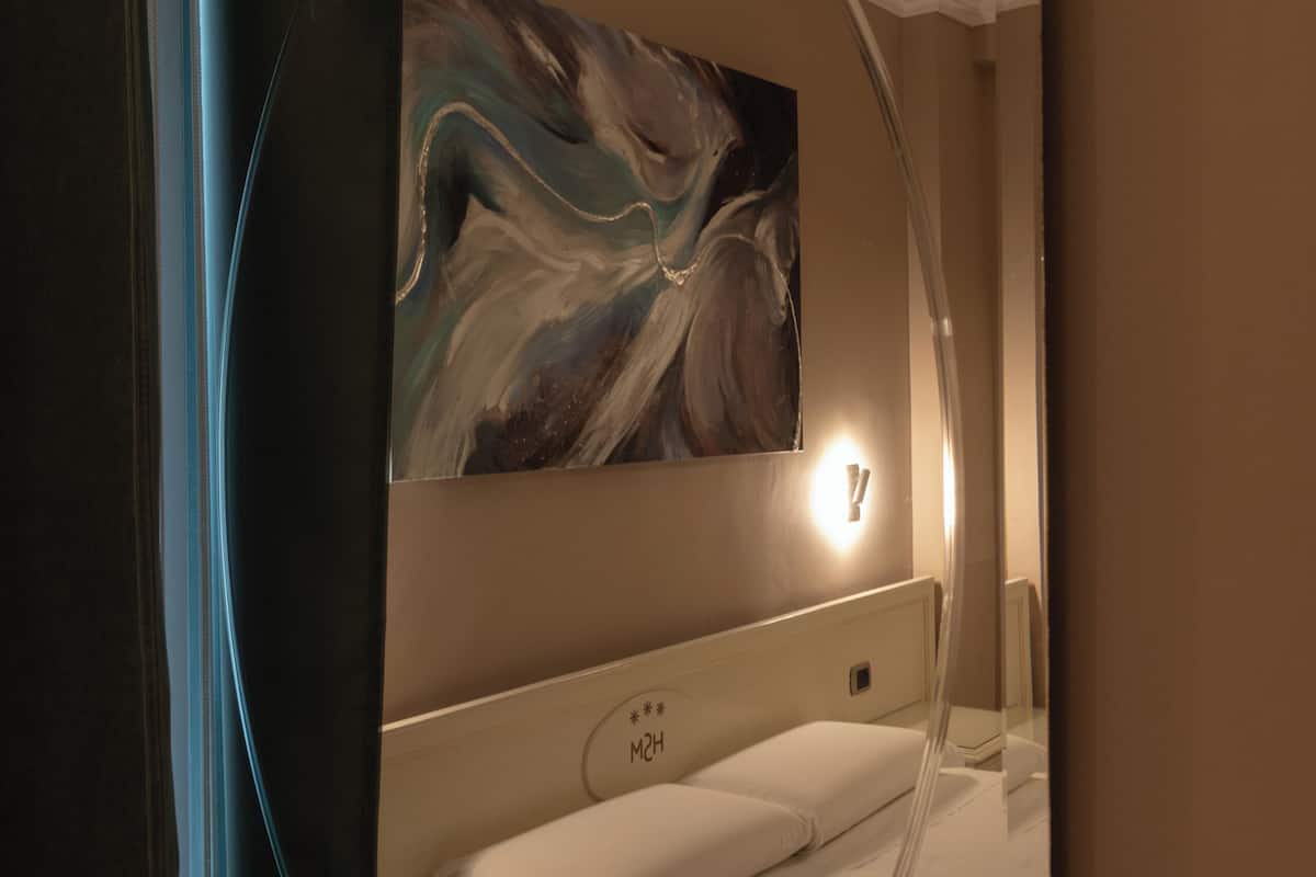 Una habitación de hotel con cama, mesita de noche y una obra de arte colgada en la pared.