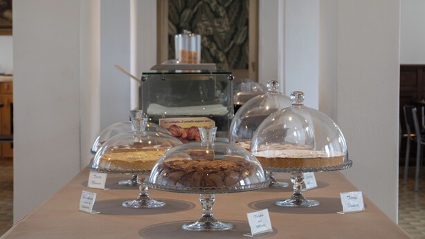 A dessert display with various cakes under glass domes, labeled with names. - Hotel Santa Maura (Rome)