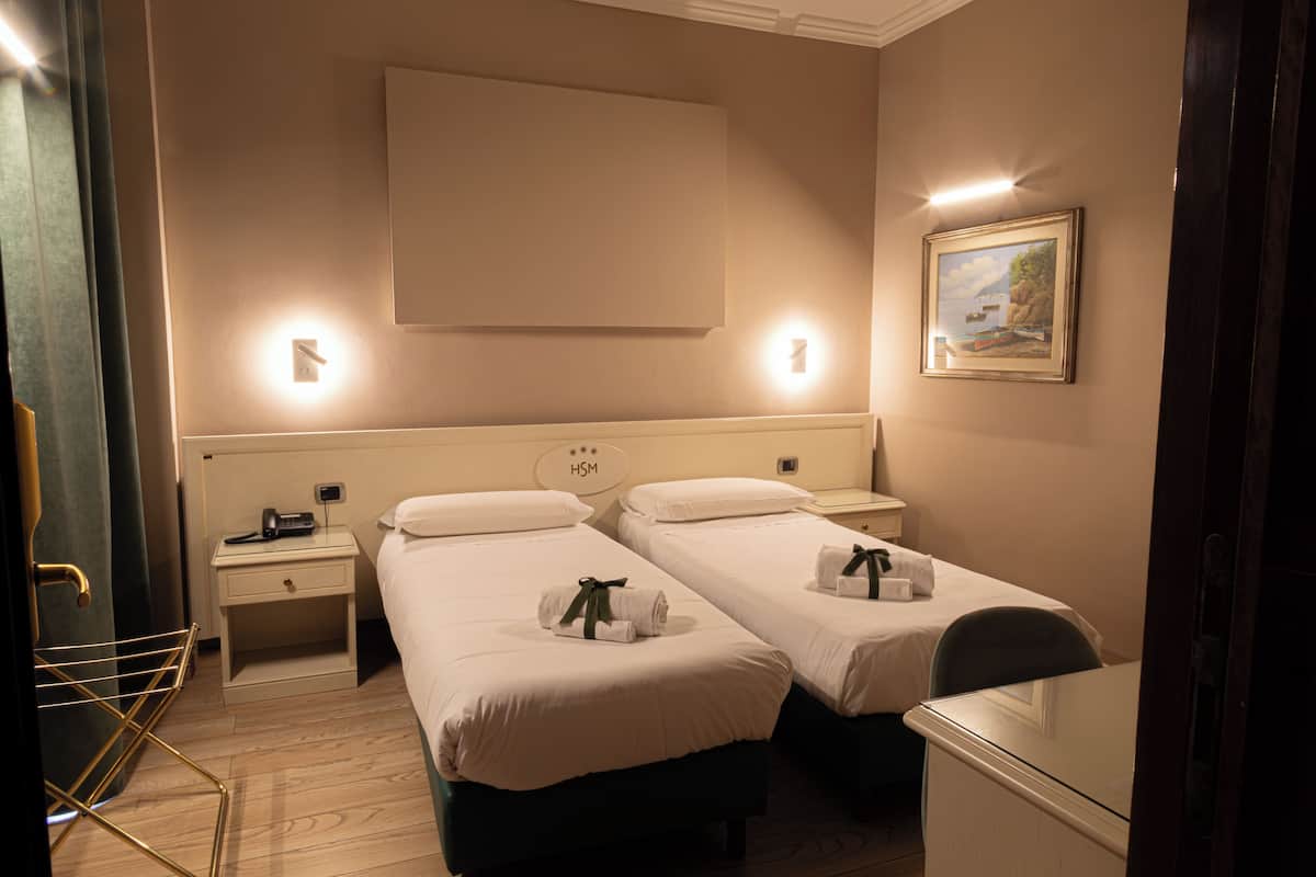 Habitación de hotel con dos camas, una mesita de noche con teléfono, un televisor montado en la pared y un cuadro.