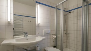 A bathroom with a sink, toilet, and glass-enclosed shower. - 1-raum-appartement mit Balkon (Seebad Heringsdorf)