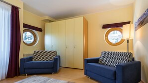A cozy room with two blue sofas, a large wardrobe, and a round window with a view. - Appartement mit 1 Schlafzimmer und Balkon (Seebad Heringsdorf)