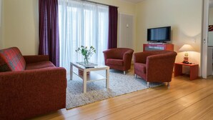 A living room with a sofa, two armchairs, a coffee table, a TV, and a lamp. - Appartement mit 1 Schlafzimmer und Balkon (Seebad Heringsdorf)