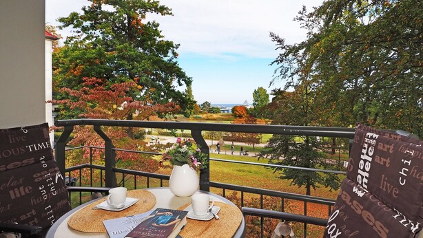 A balcony with a table set for two, featuring a book and a vase with flowers. - Appartement mit 1 Schlafzimmer und Balkon (Seebad Heringsdorf)
