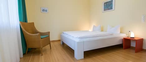 A room with a bed, a chair, a nightstand, and a wall-mounted picture.