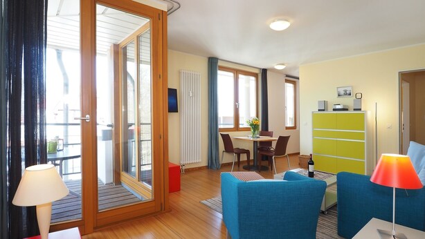 Ein modernes Wohnzimmer mit Holzboden, einem Essbereich mit Tisch und Stühlen, einer Couch, einem roten Schrank und einer Lampe.