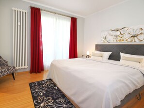 Ein Schlafzimmer mit einem großen Bett, einem Sessel, einem Heizkörper und einem Fenster mit Vorhängen.