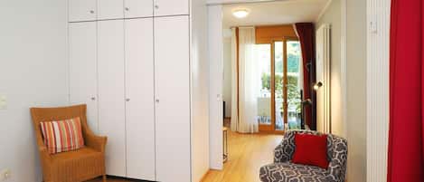A bedroom with a bed, a wardrobe, a chair, and a view of the outside.