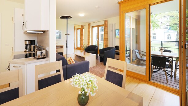 A modern kitchen with appliances, a dining area with a table and chairs, and a balcony with outdoor furniture. - Apartment with 2 bedrooms and balcony (Seebad Heringsdorf)