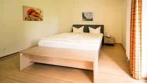 A bedroom with a bed, a nightstand, a wall-mounted painting, and a window with curtains. - Apartment with 2 bedrooms and balcony (Seebad Heringsdorf)